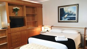 A hotel room with a large bed, a television, wooden built-in shelving, and a painting of a sailboat. - Cosmos Hotel (Caxias do Sul)