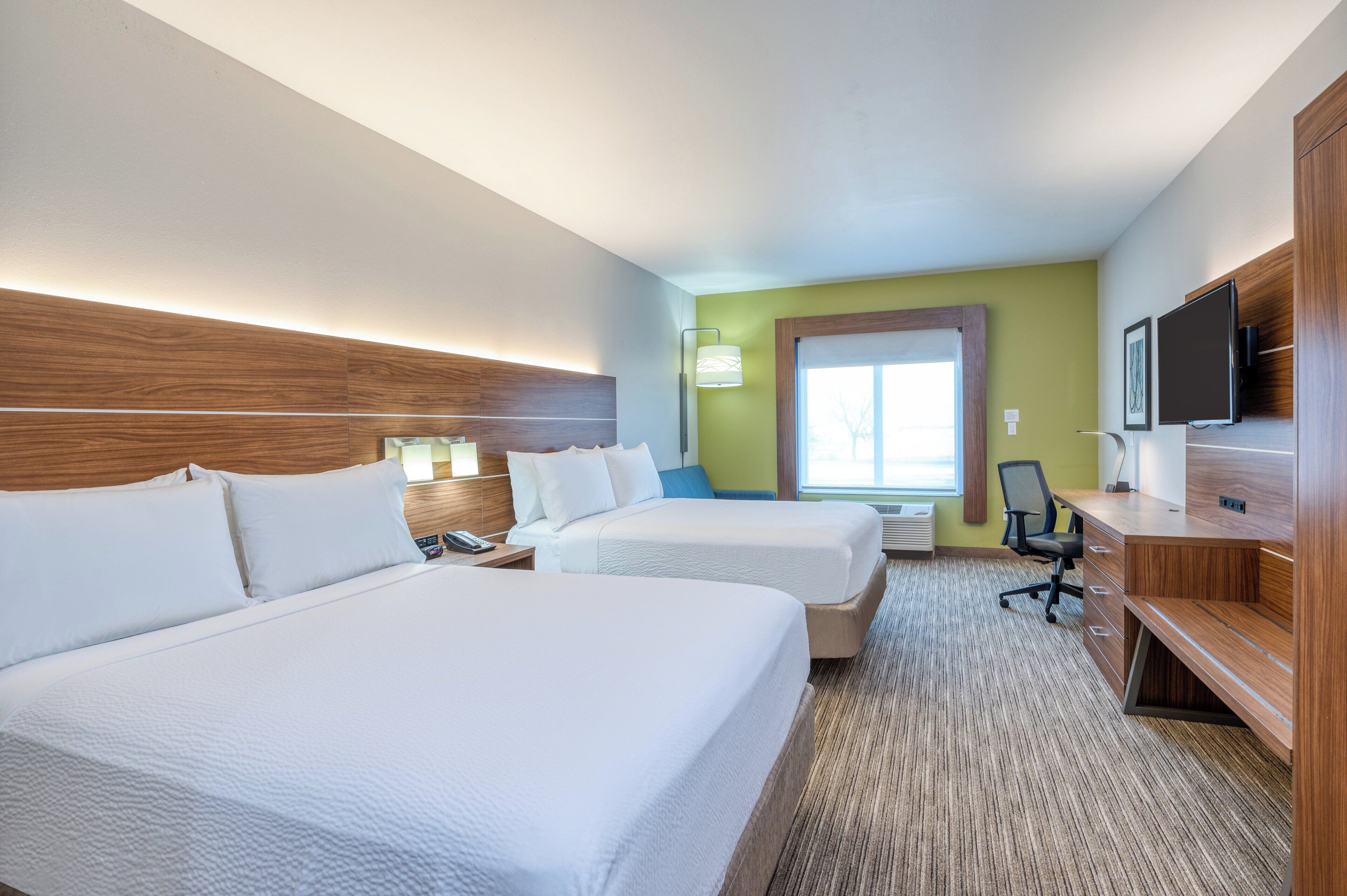 A hotel room with two beds, a desk, a chair, a TV, and a window.