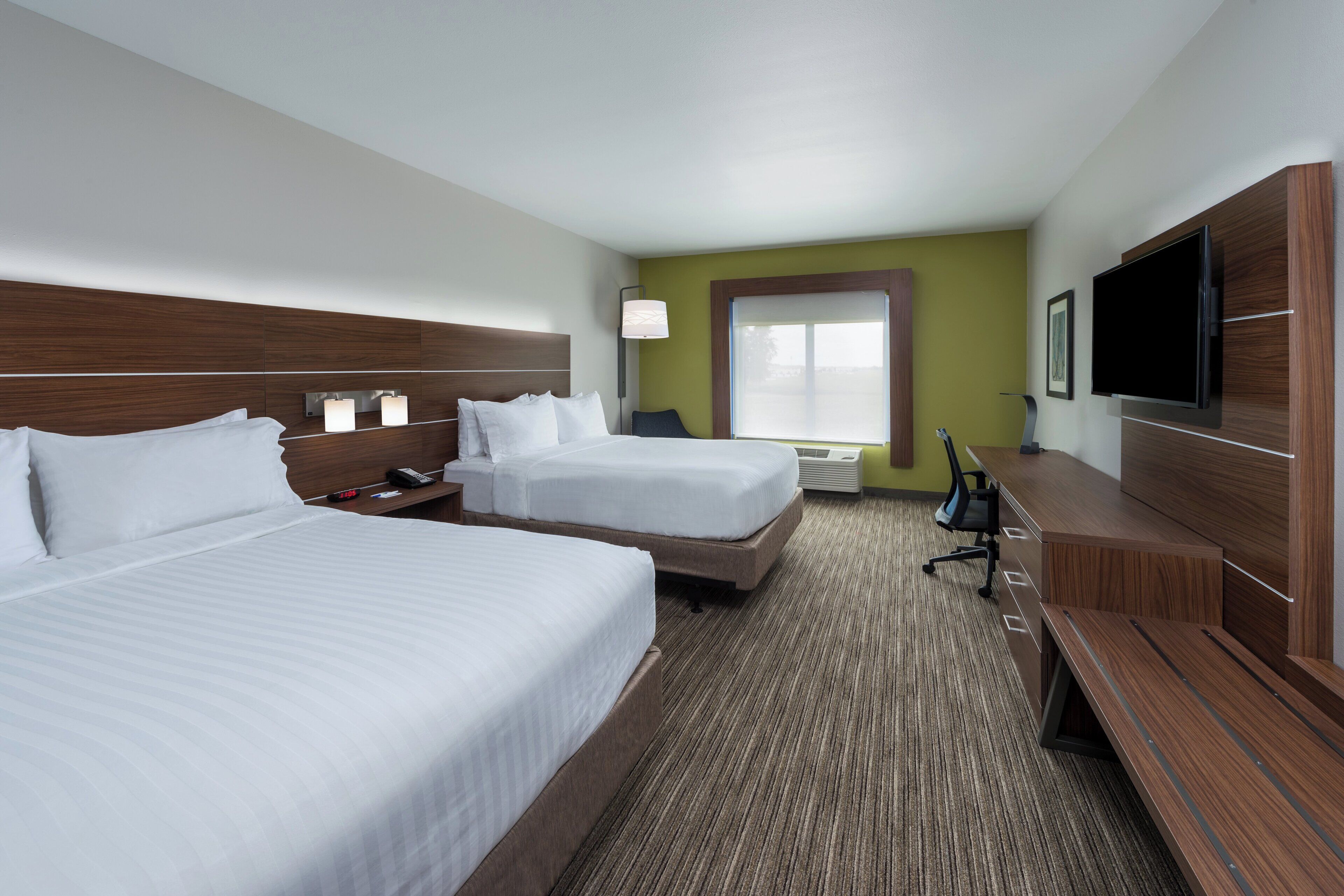 A hotel room with two beds, a TV, a desk, and a window.
