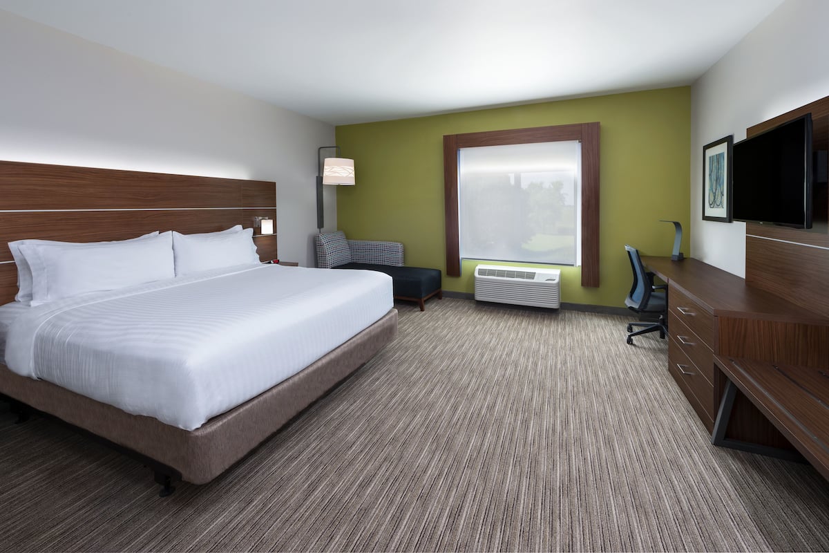 A hotel room with a large bed, a desk with a chair, a flat-screen TV, and a window with blinds.