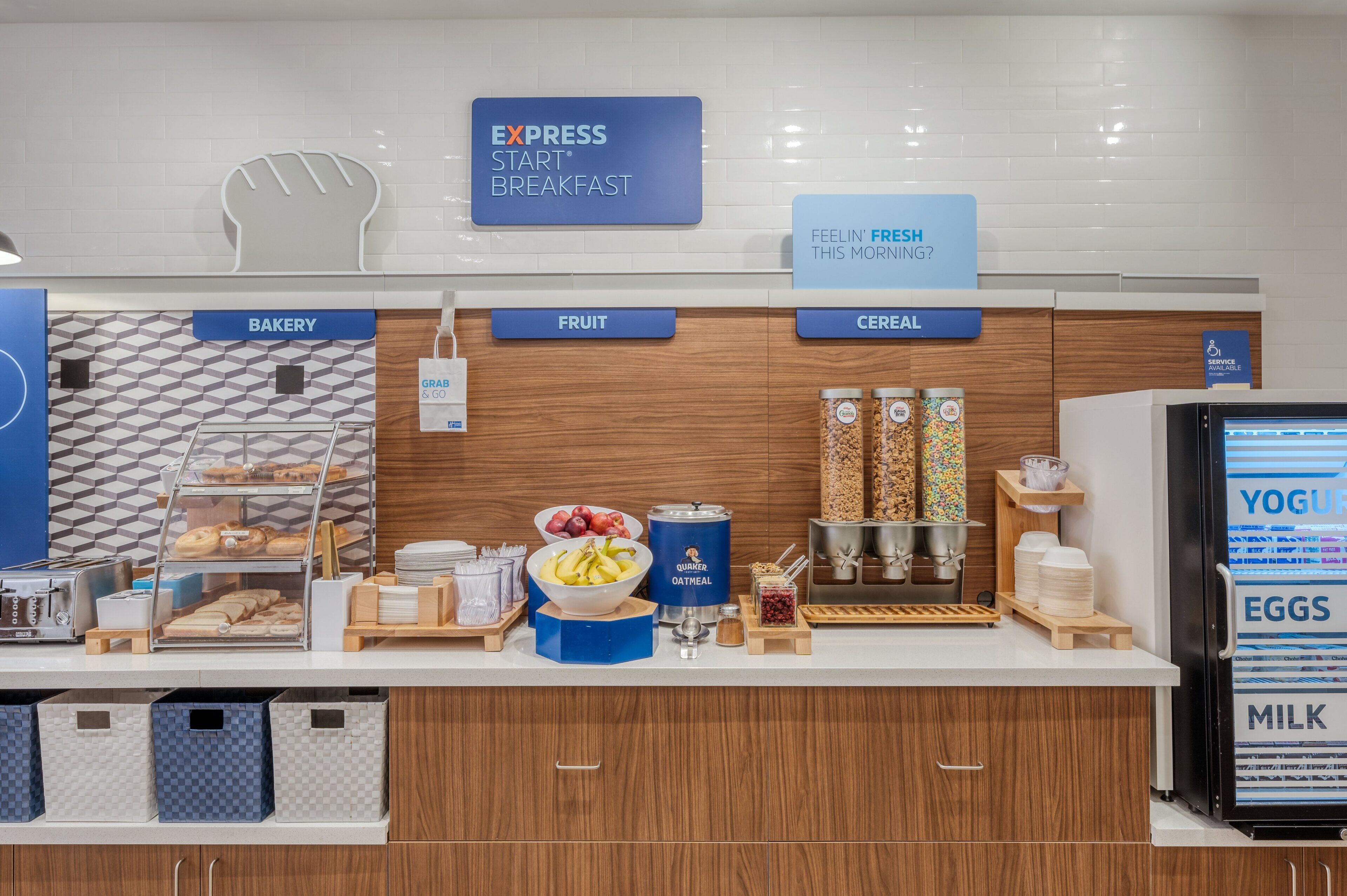 A breakfast station with labeled sections for bakery, fruit, and cereal, including a display of pastries, fruits, and cereal containers.