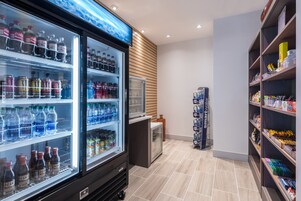 A beverage refrigerator stocked with various drinks, a television mounted on the wall, and shelves with snacks and bottled water.