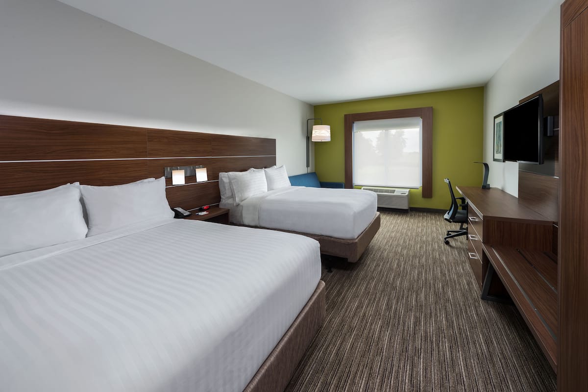 A hotel room with two beds, a desk, a chair, a TV, and a window.