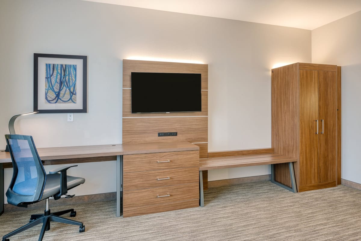 A modern room with a wooden desk, a flat-screen TV, a framed abstract artwork, and a wardrobe.
