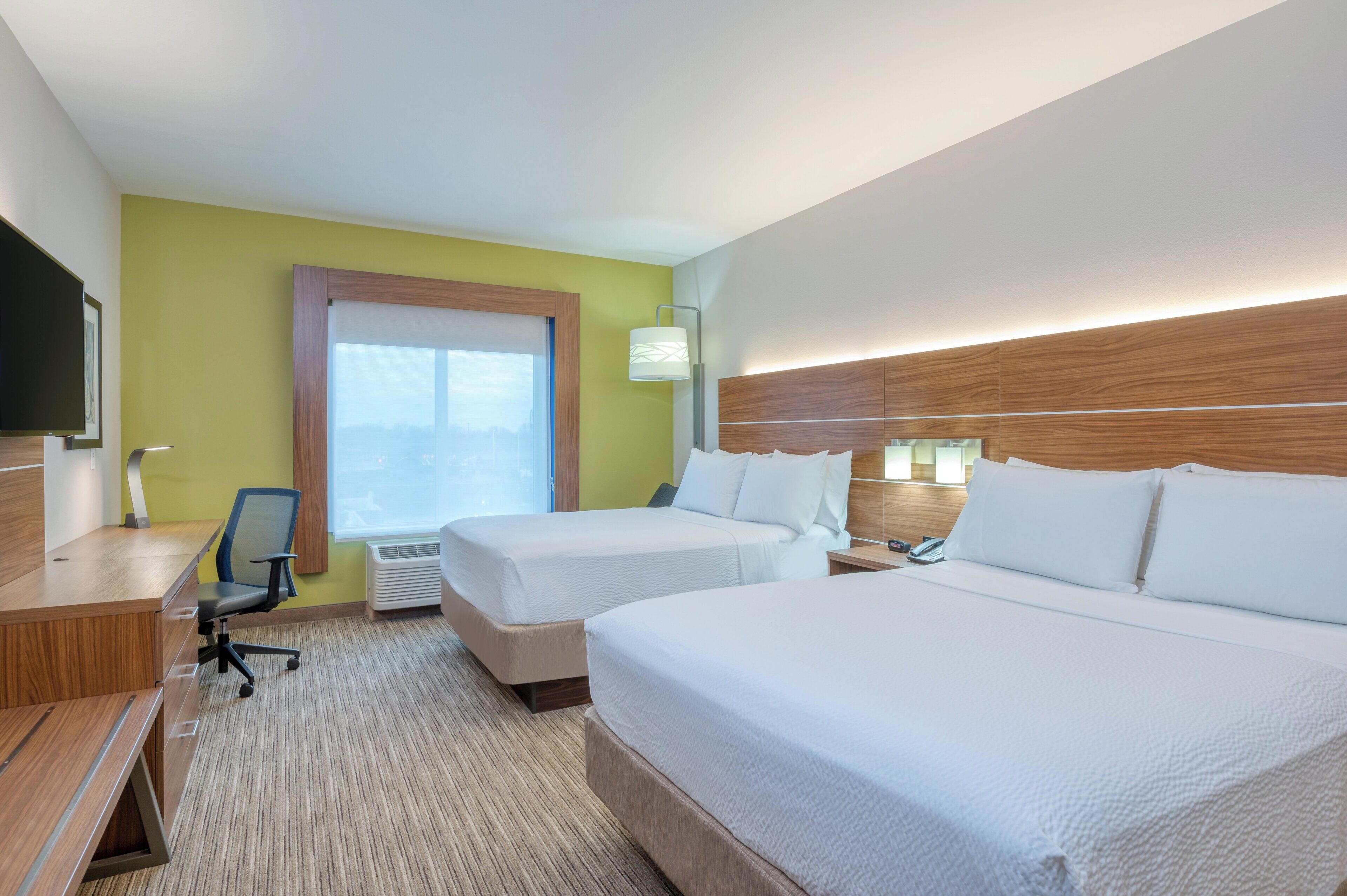 Een hotelkamer met twee bedden, een bureau, een stoel, een televisie en een raam met zonwering.