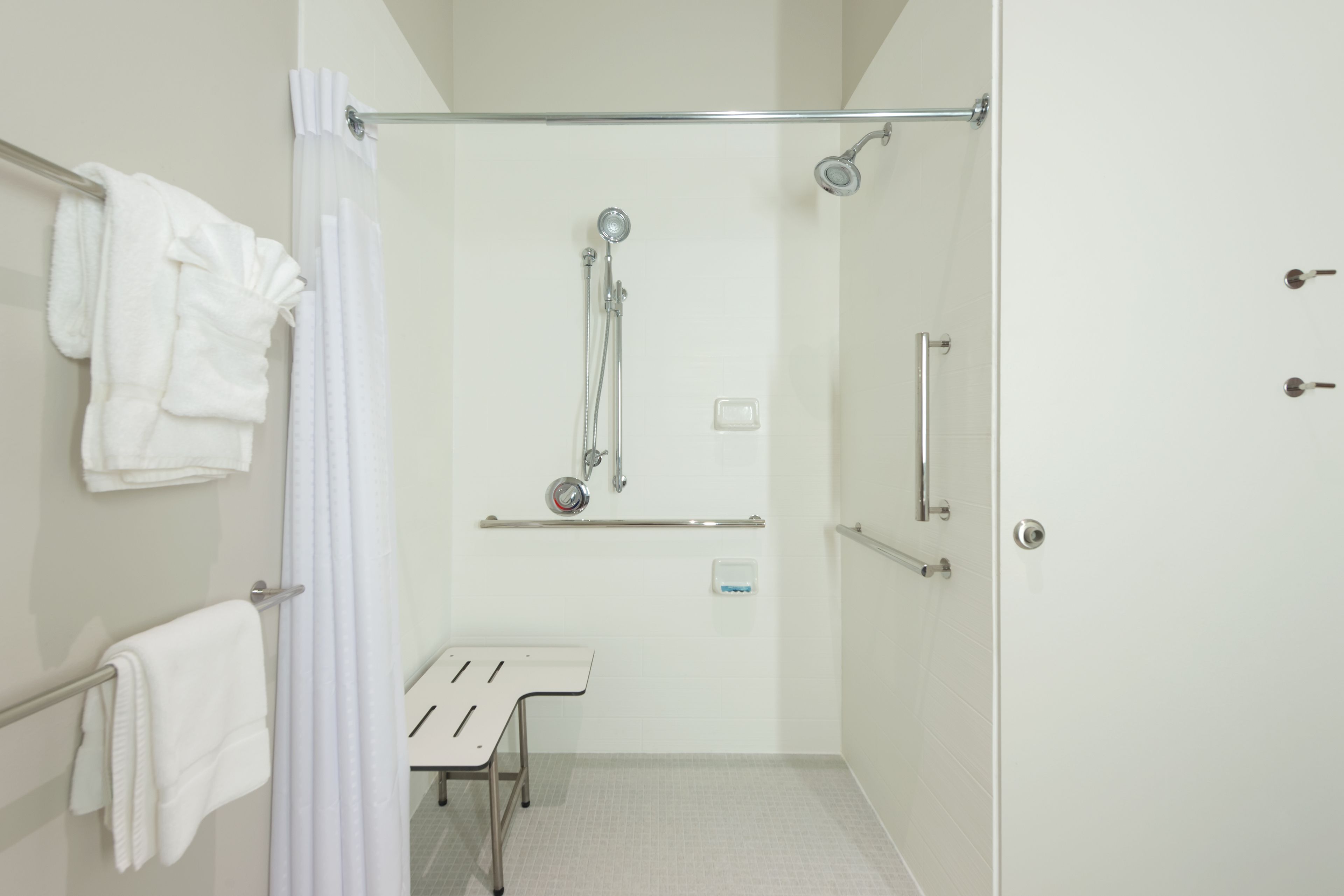 Une salle de bain équipée d’une douche, de barres d’appui, d’un banc et de serviettes blanches.