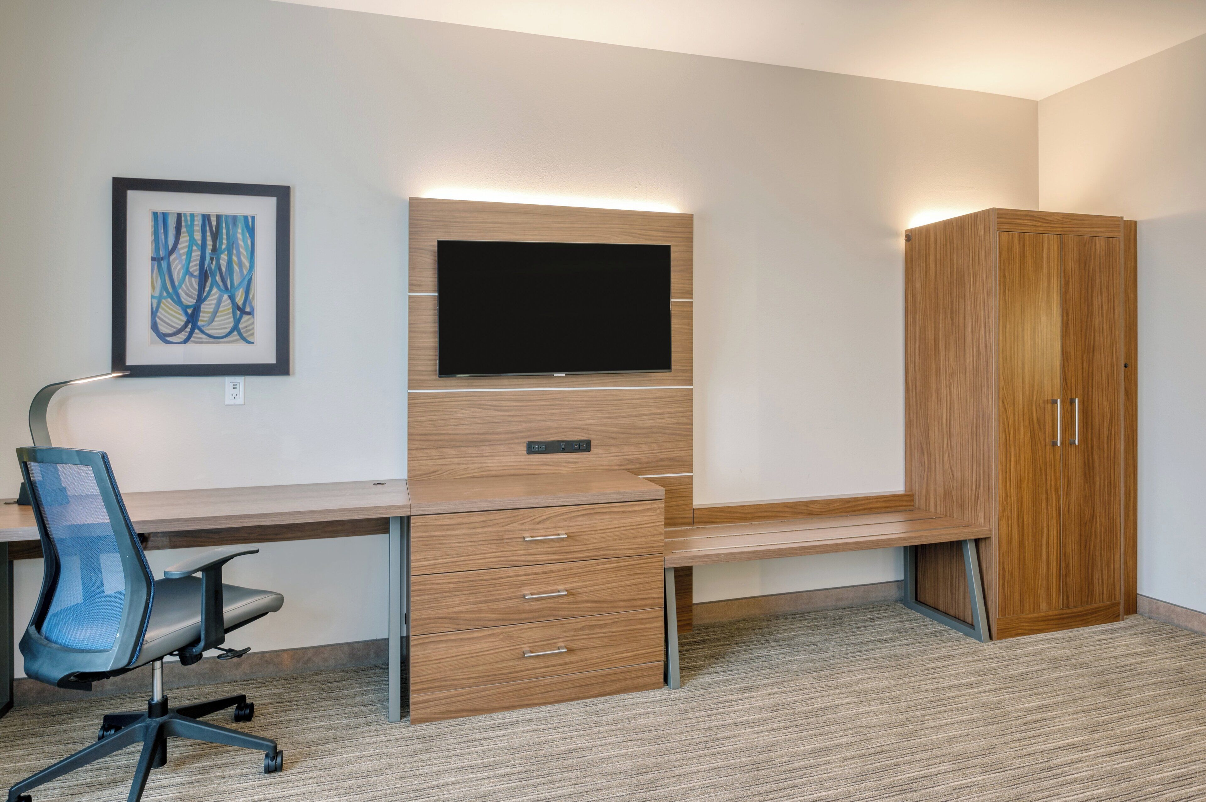 A modern office space with a desk, chair, TV, and wardrobe.