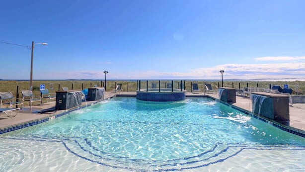 Una piscina azul cristalina con un jacuzzi central, rodeada de sillones de descanso y un paisaje desértico al fondo.