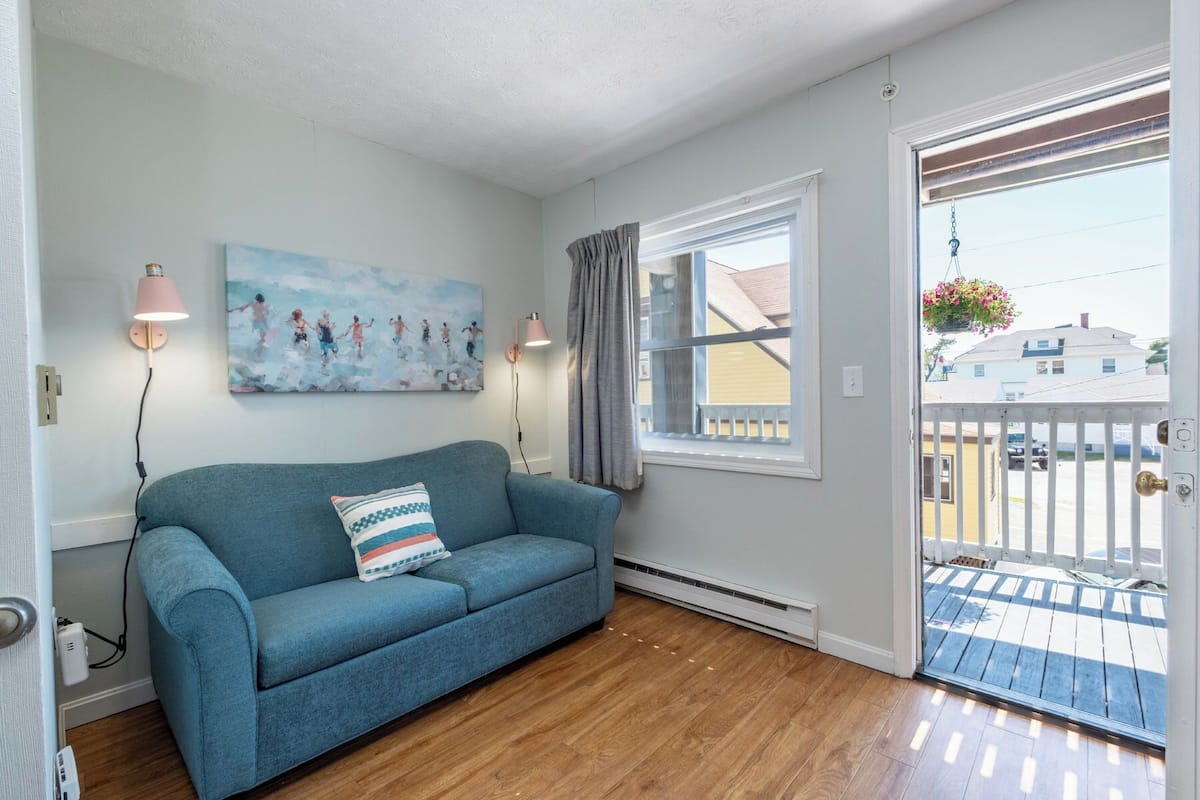 A room with a blue sofa, a painting, two wall lamps, a window with curtains, and a door leading to an outdoor area.