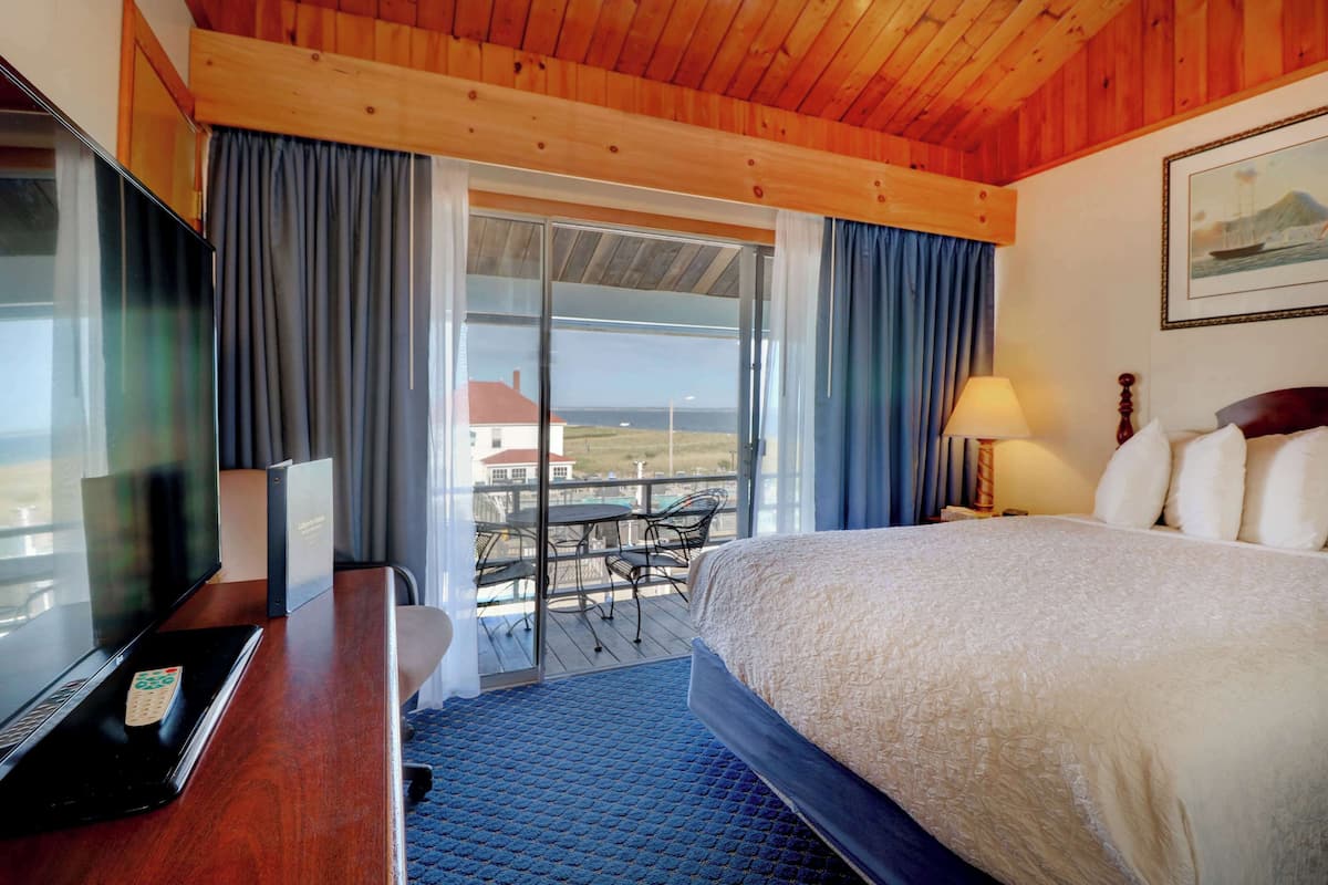 A hotel room with a bed, a desk with a laptop, a TV, and a balcony with a table and chairs.