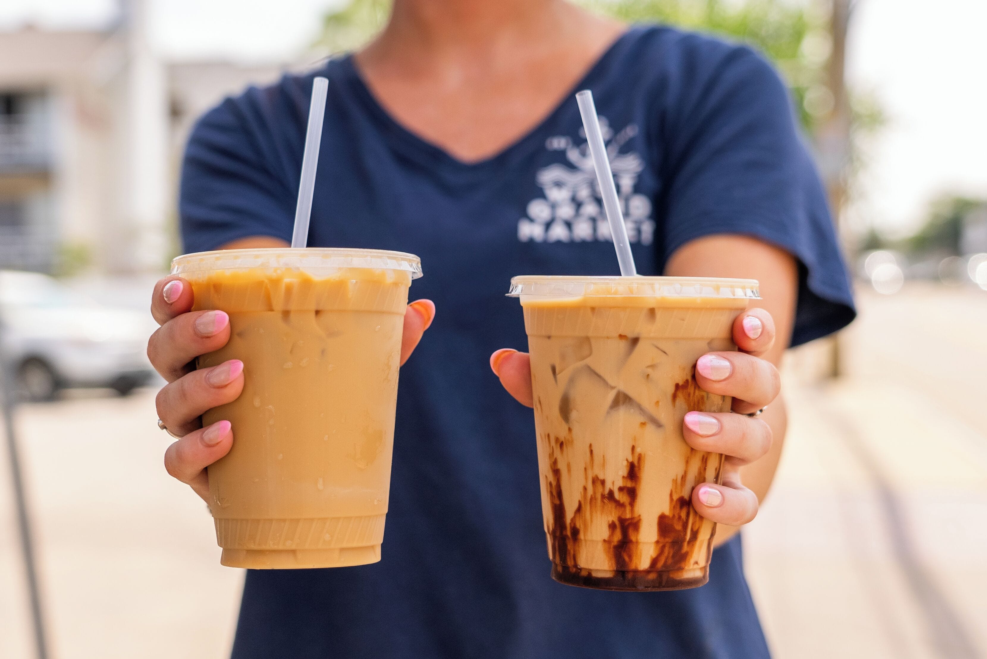 Une personne tenant deux gobelets de café glacé, l’un muni d’une paille et l’autre non, dans un cadre extérieur.
