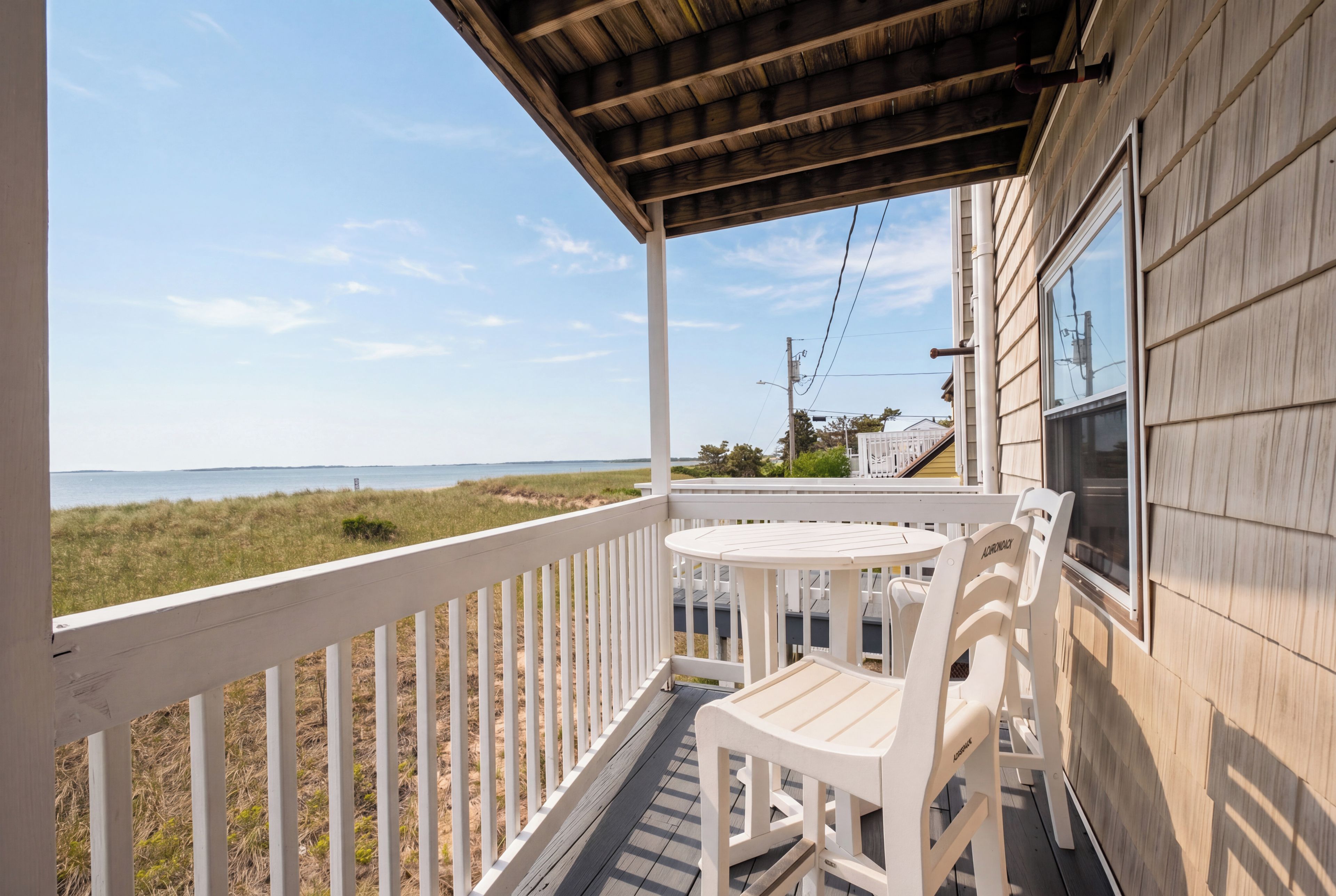 A covered porch with a table and chairs, overlooking a beach.
