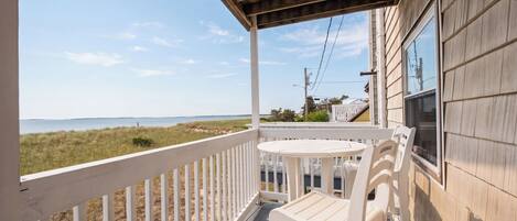 A covered porch with a table and chairs, overlooking a beach.