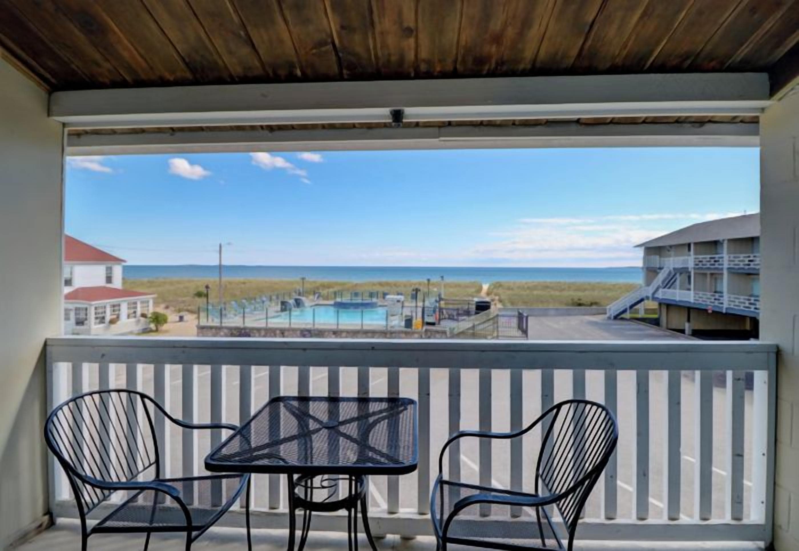 A balcony with two chairs and a table, overlooking a beach and a pool area.