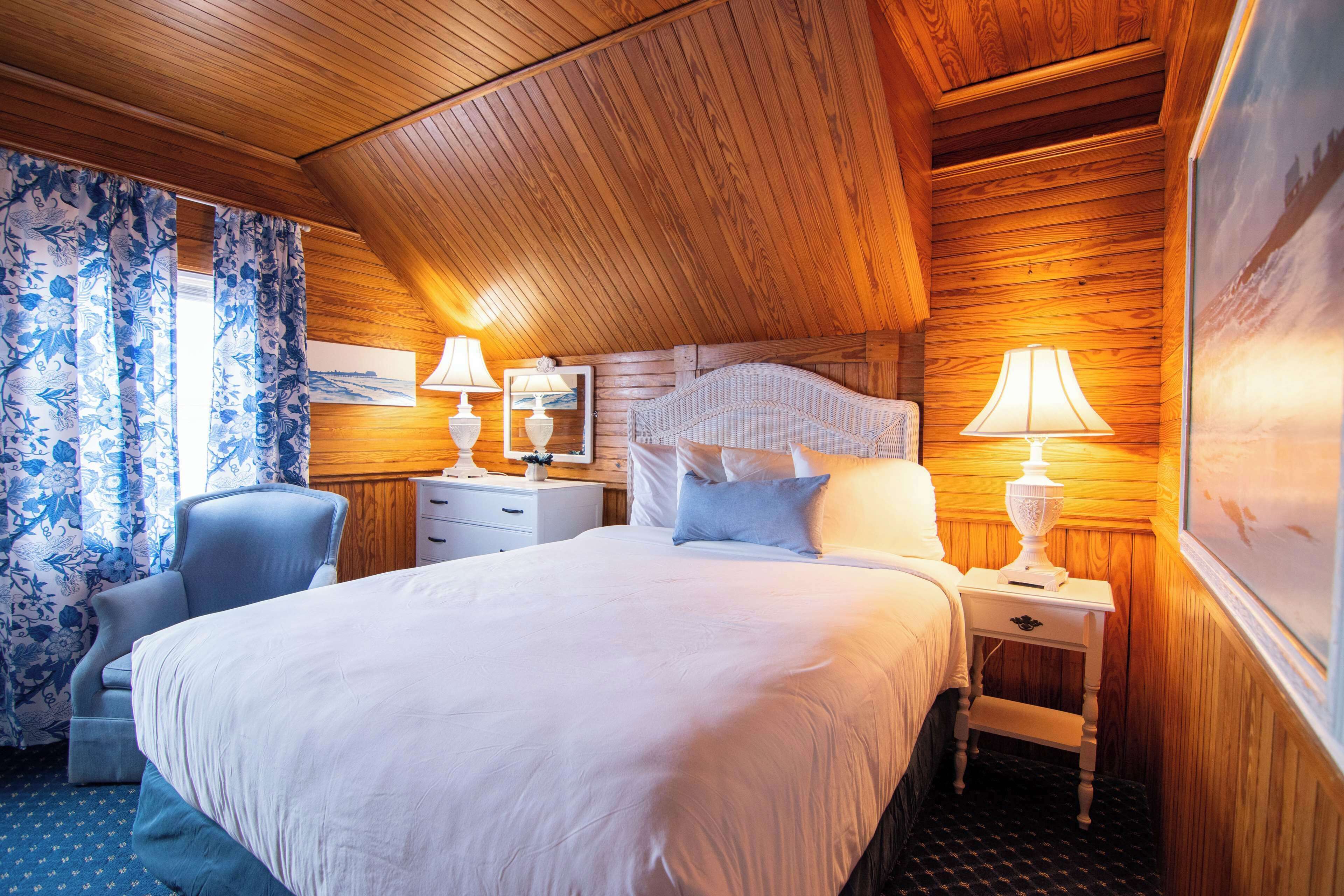 Une chambre à coucher avec un grand lit, deux tables de chevet, une chaise et un lambris en bois.