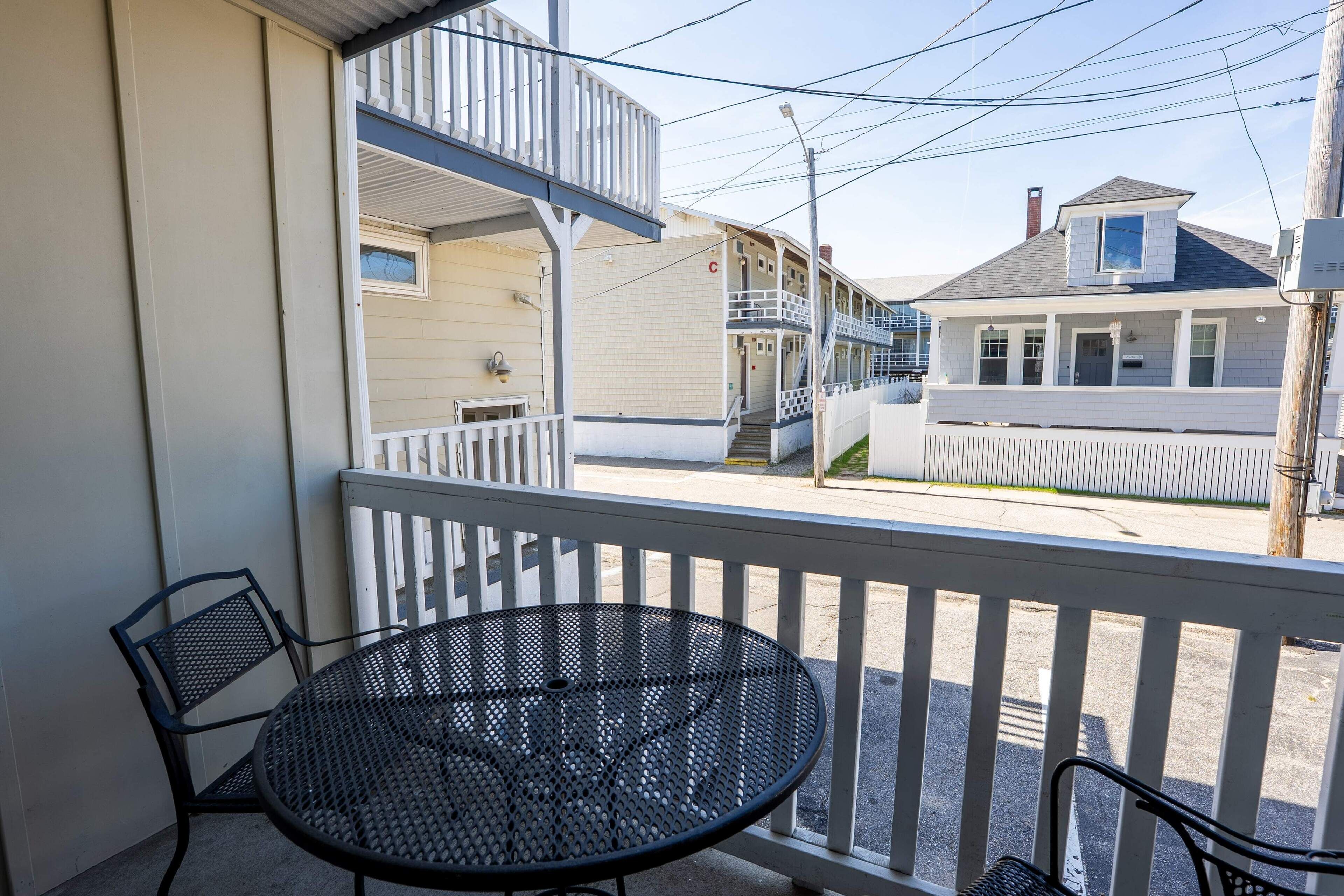 A balcony with a metal table and chairs, overlooking a street with buildings.
