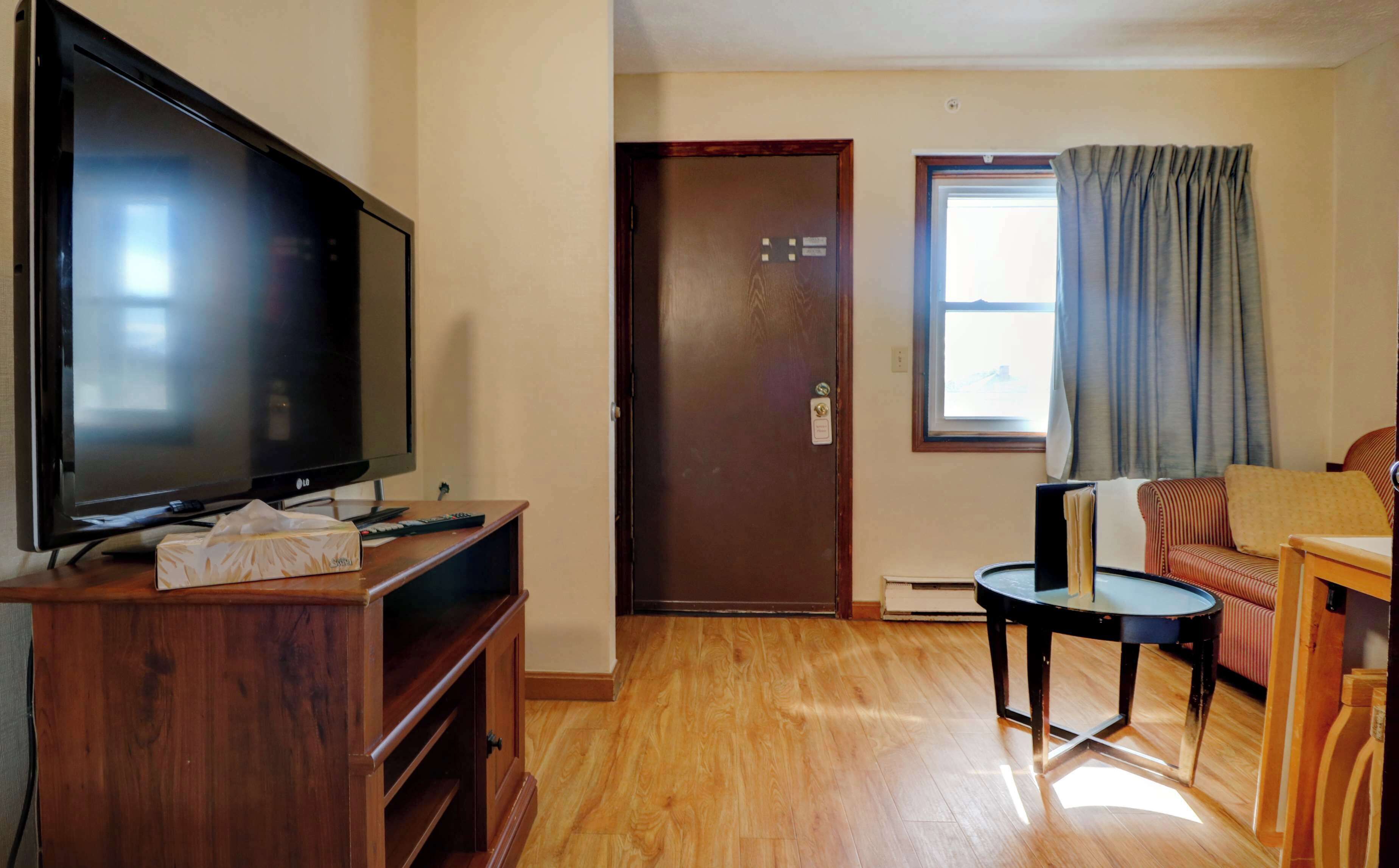 Una sala de estar con una televisión de pantalla plana, piso de madera, una puerta, una ventana con cortinas y un sofá a rayas.