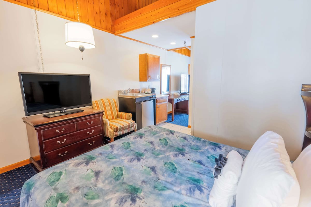 A hotel room with a bed, a TV, a desk, and a bathroom visible through an open door.