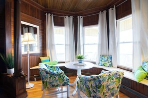 A room with wooden paneled walls, a round white table, two patterned chairs, a floor lamp, and a window seat with cushions. - Waves Oceanfront Resort (Old Orchard Beach)