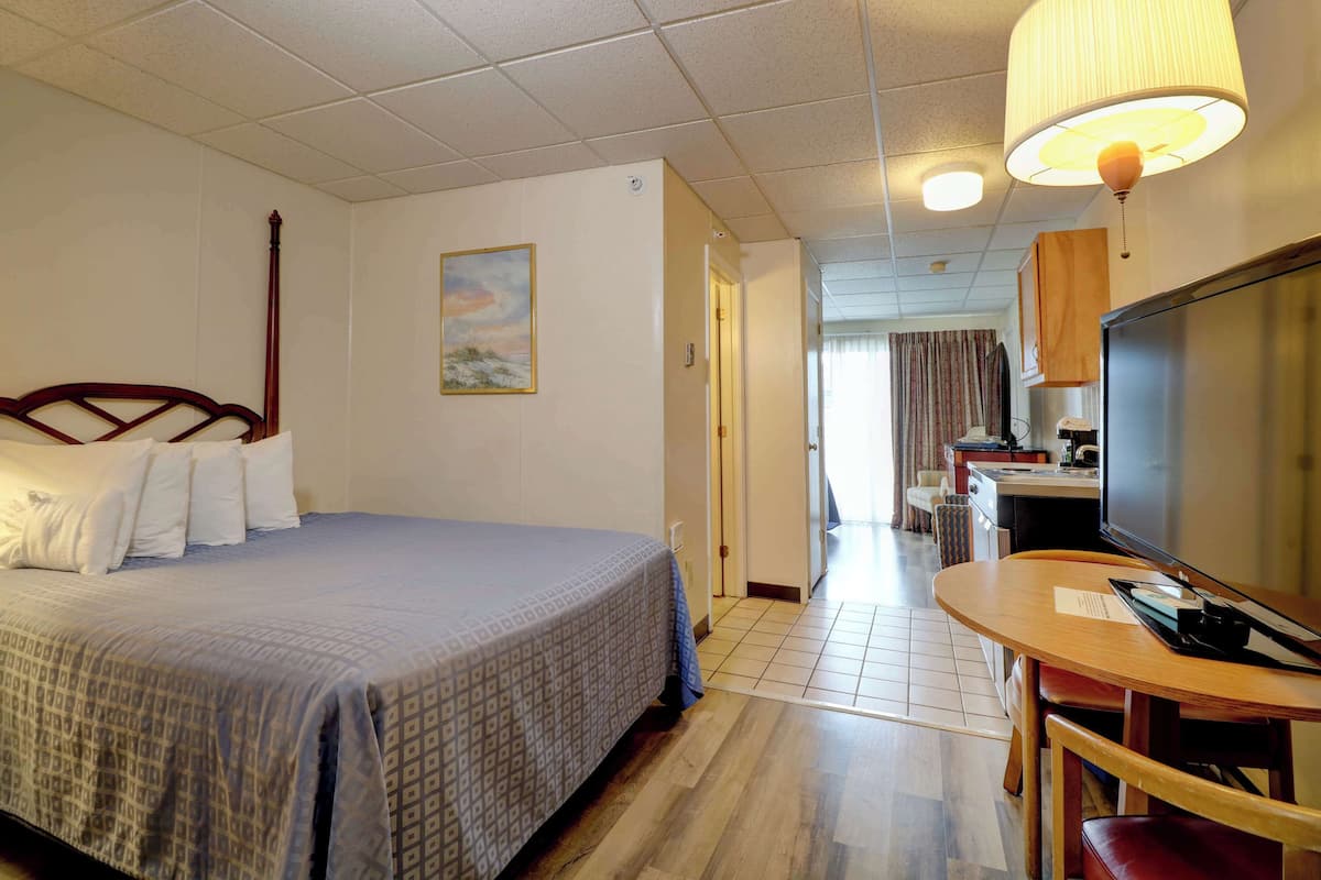 A hotel room with a bed, a desk with a chair, a television, and a kitchenette area.