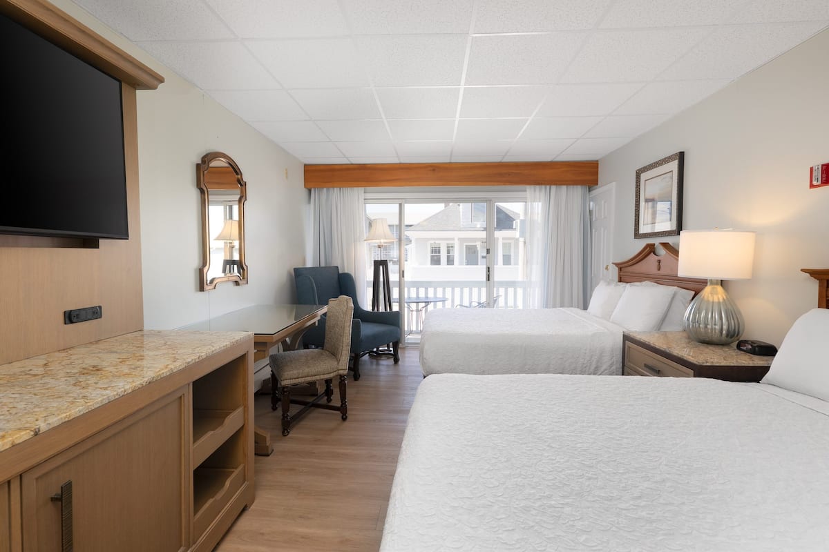 A hotel room with two beds, a desk, a chair, a television, and a window with a view of buildings.