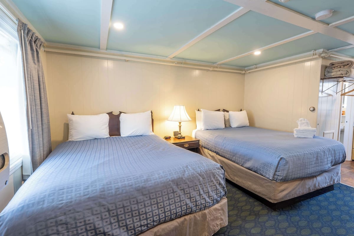 A hotel room with two beds, a nightstand with a lamp, and a window with curtains.