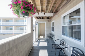 A balcony with a hanging flower basket, a door leading to an interior space, and a view of a building with balconies.