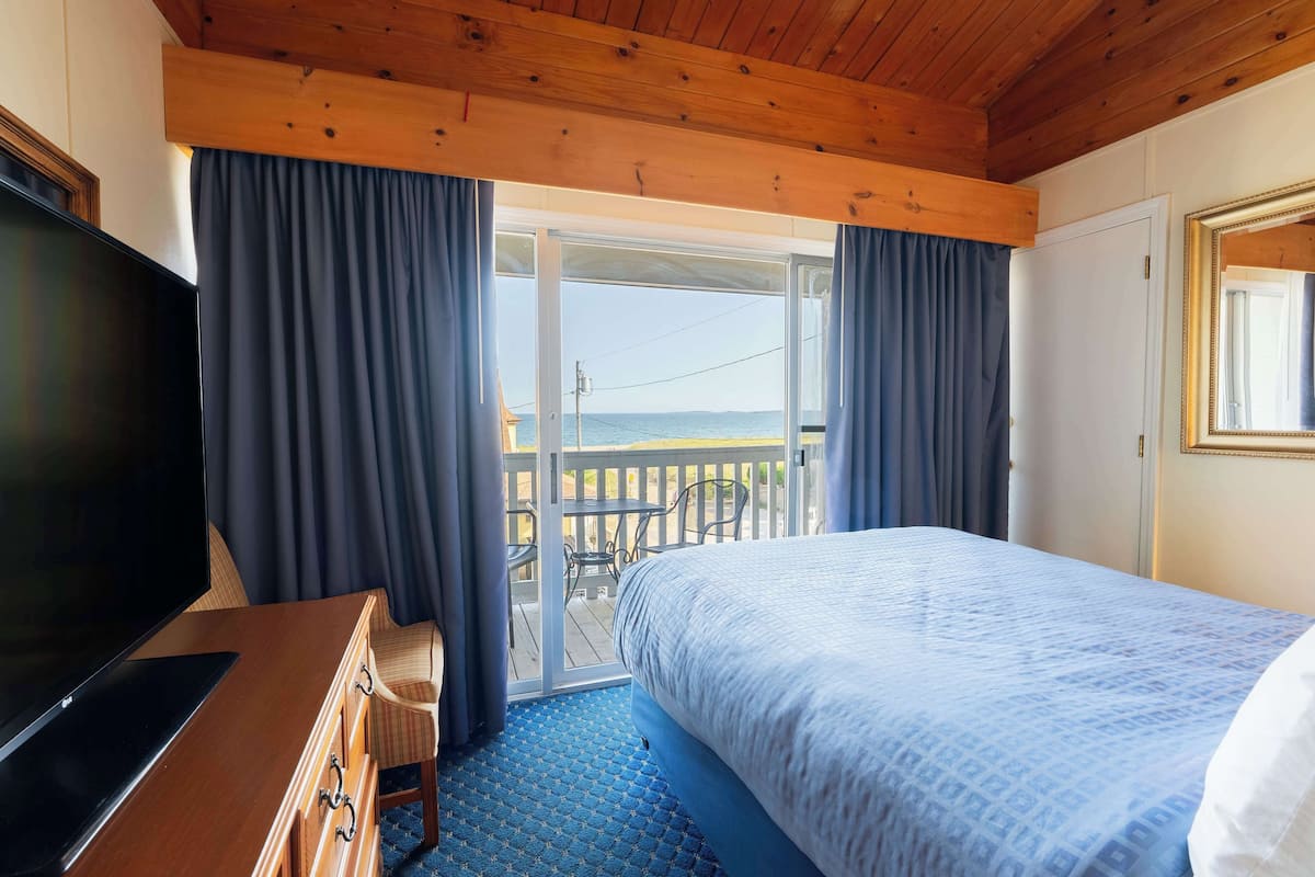 A hotel room with a bed, a TV, a wooden desk, and a balcony with a view of the sea.