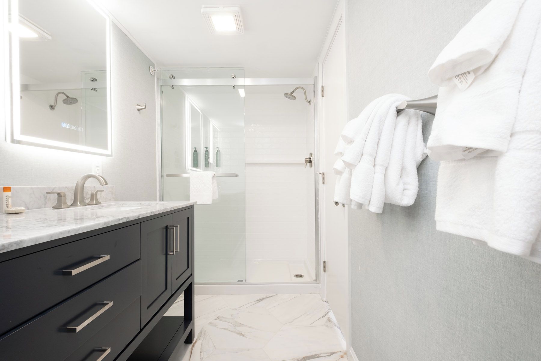 A modern bathroom with a marble countertop, a black vanity, a glass shower enclosure, and white towels on a rack.