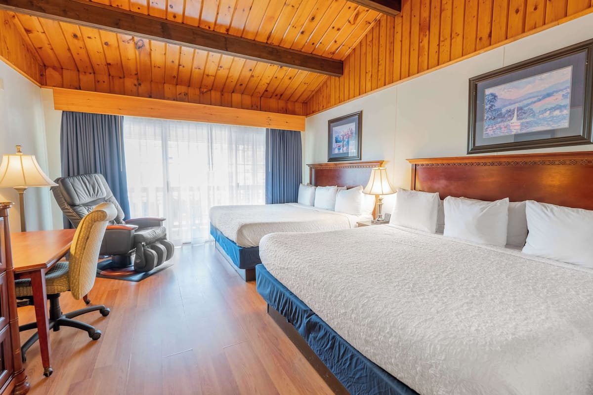 A hotel room with two beds, a desk, a chair, and a window with curtains.