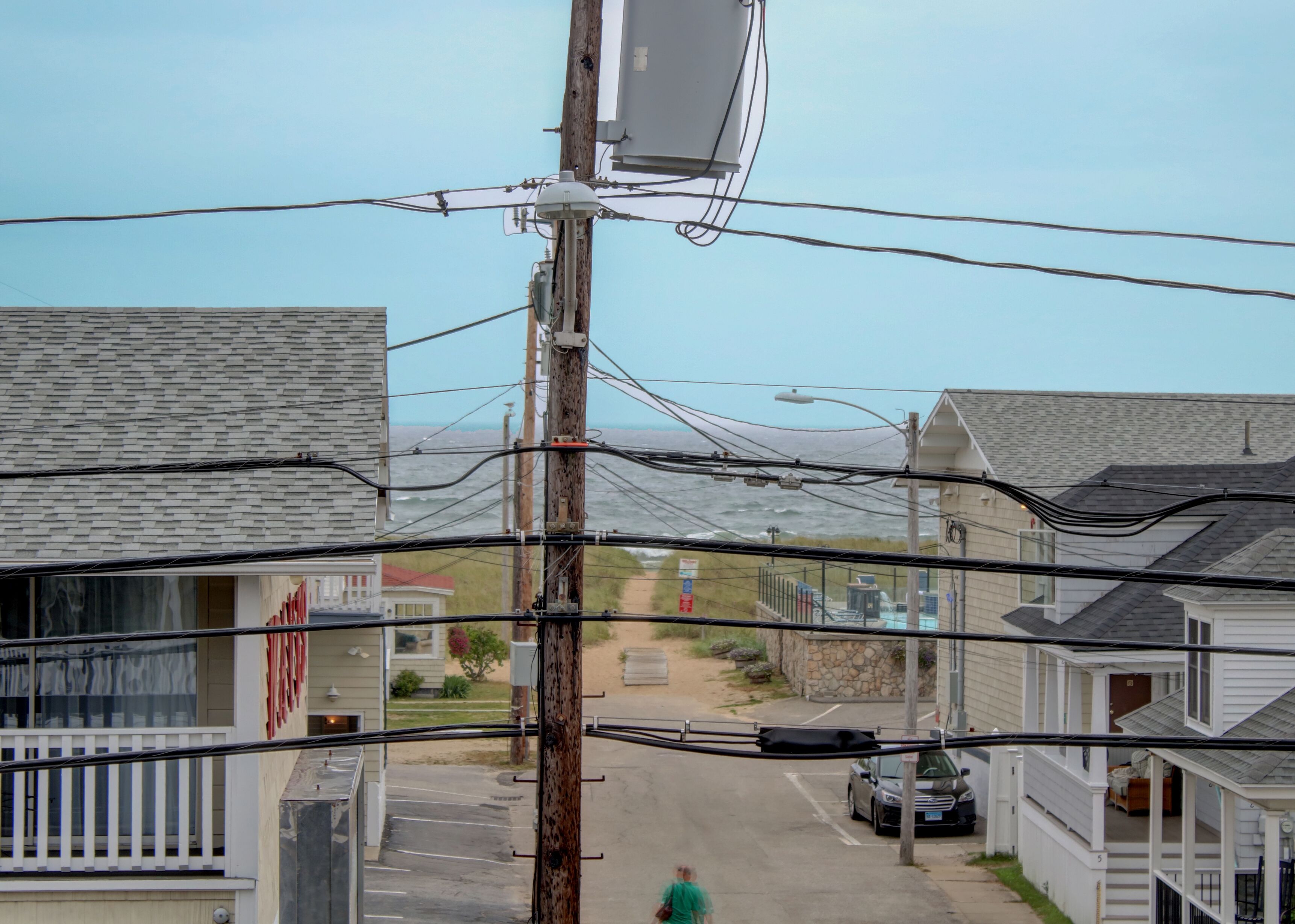 Una calle residencial con casas, un poste de electricidad y líneas de alta tensión.