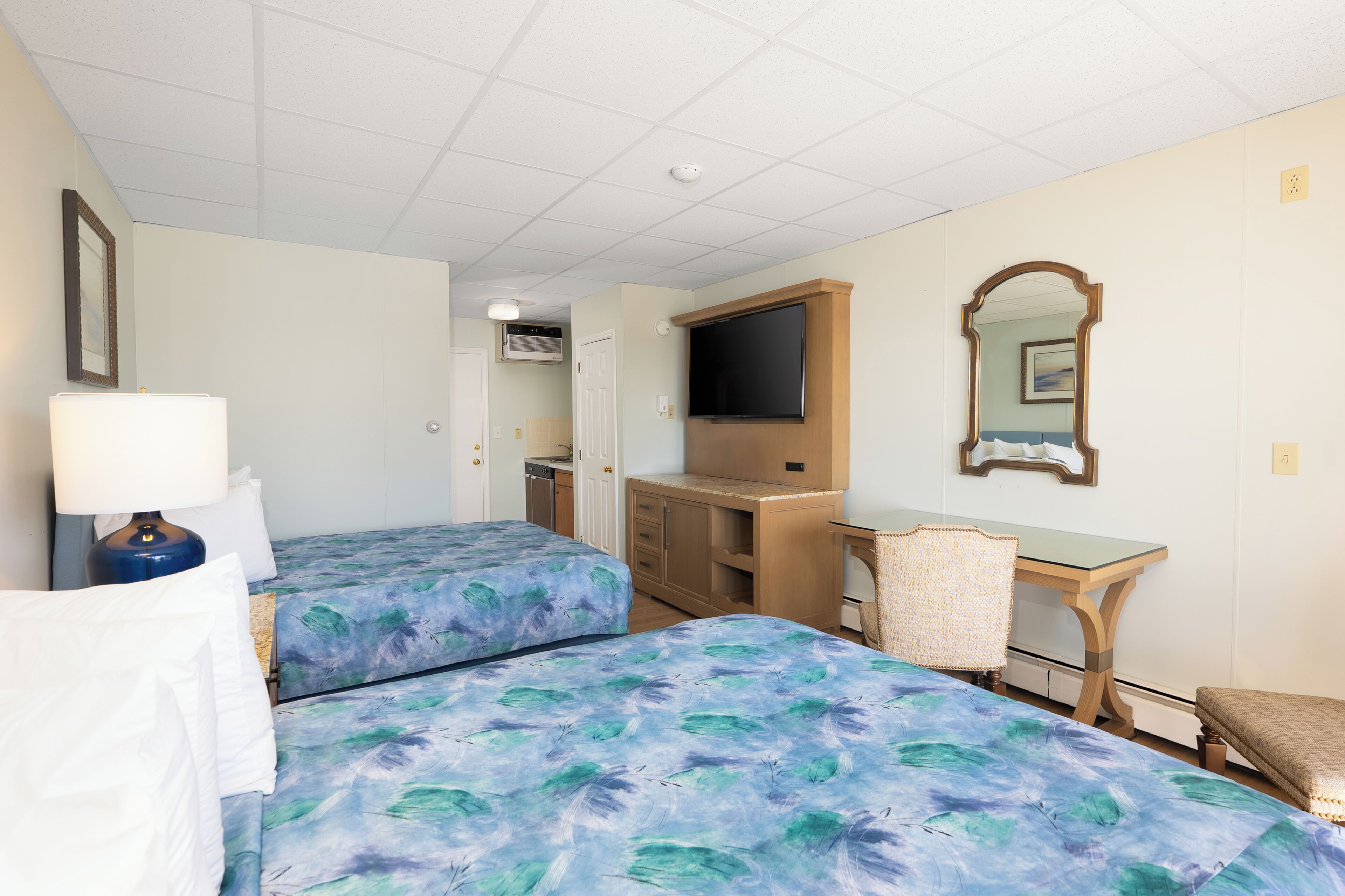 Une chambre d’hôtel avec deux lits, un bureau, une chaise, une télévision et un miroir.