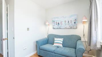 A room with a light blue sofa, a wall-mounted painting, two wall-mounted lamps, and a door.