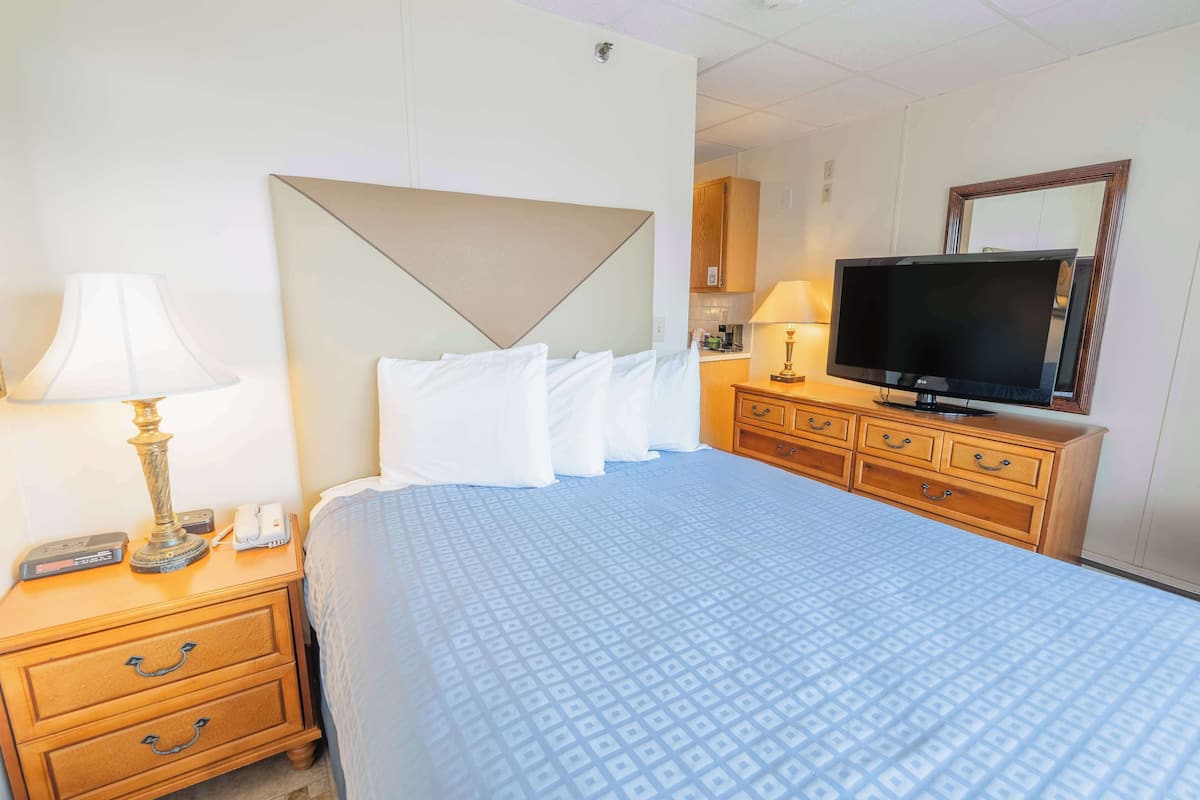 A hotel room with a bed, bedside lamps, a TV, a wooden dresser, and a mirror.