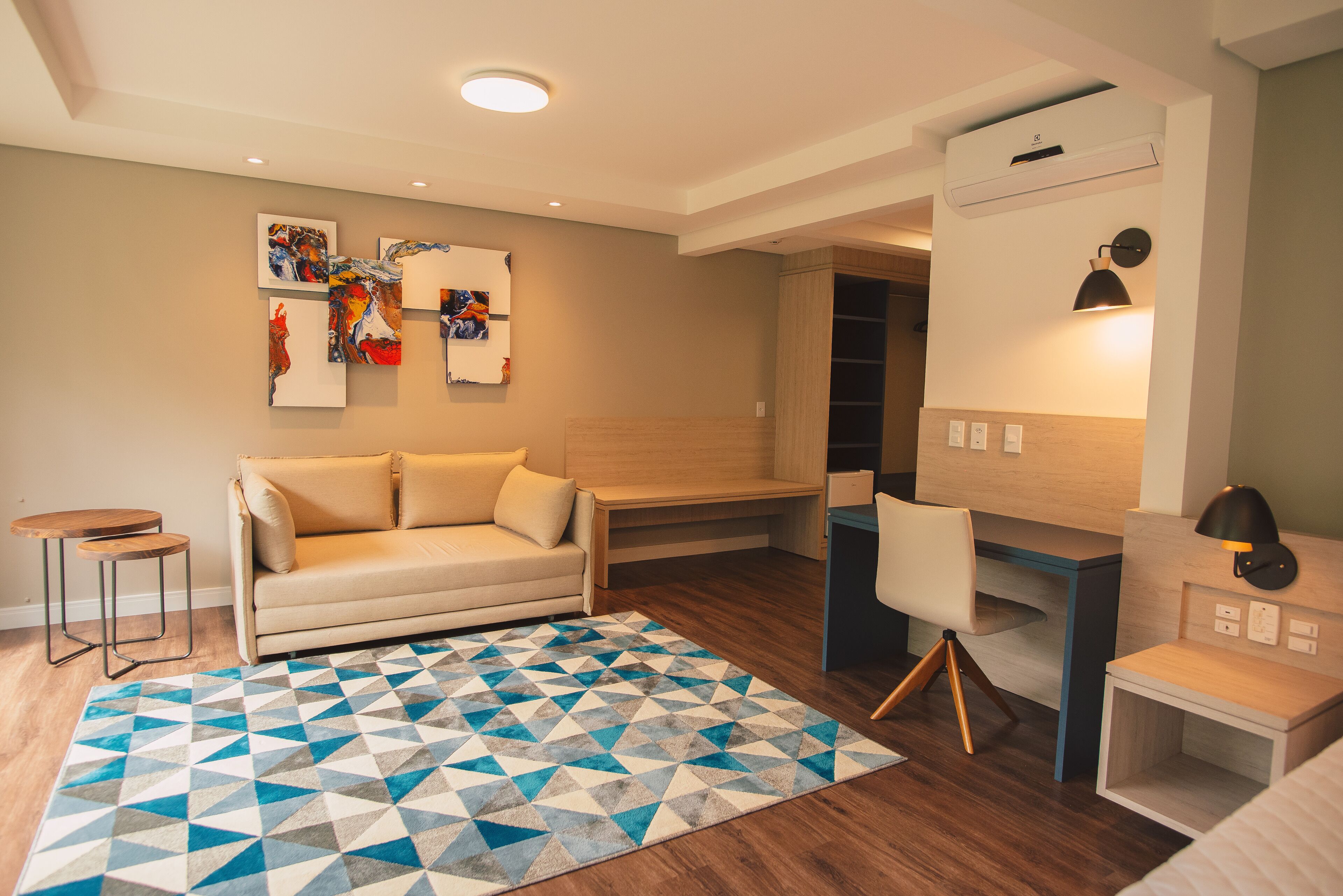 A modern living room with a sofa, a coffee table, a desk with a chair, and a patterned rug.