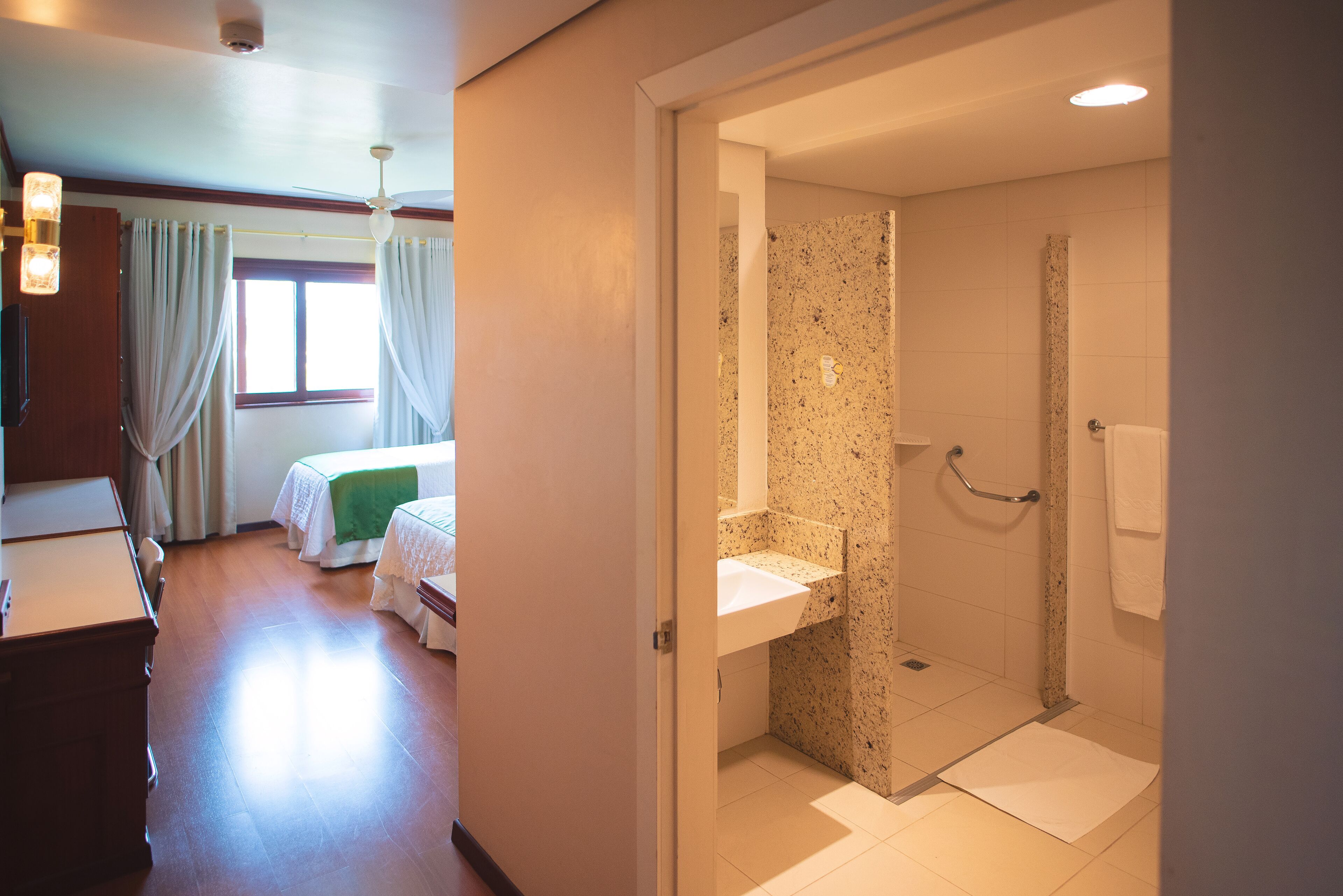Une chambre d’hôtel avec un lit, un bureau, une salle de bain avec douche et une fenêtre avec des rideaux.
