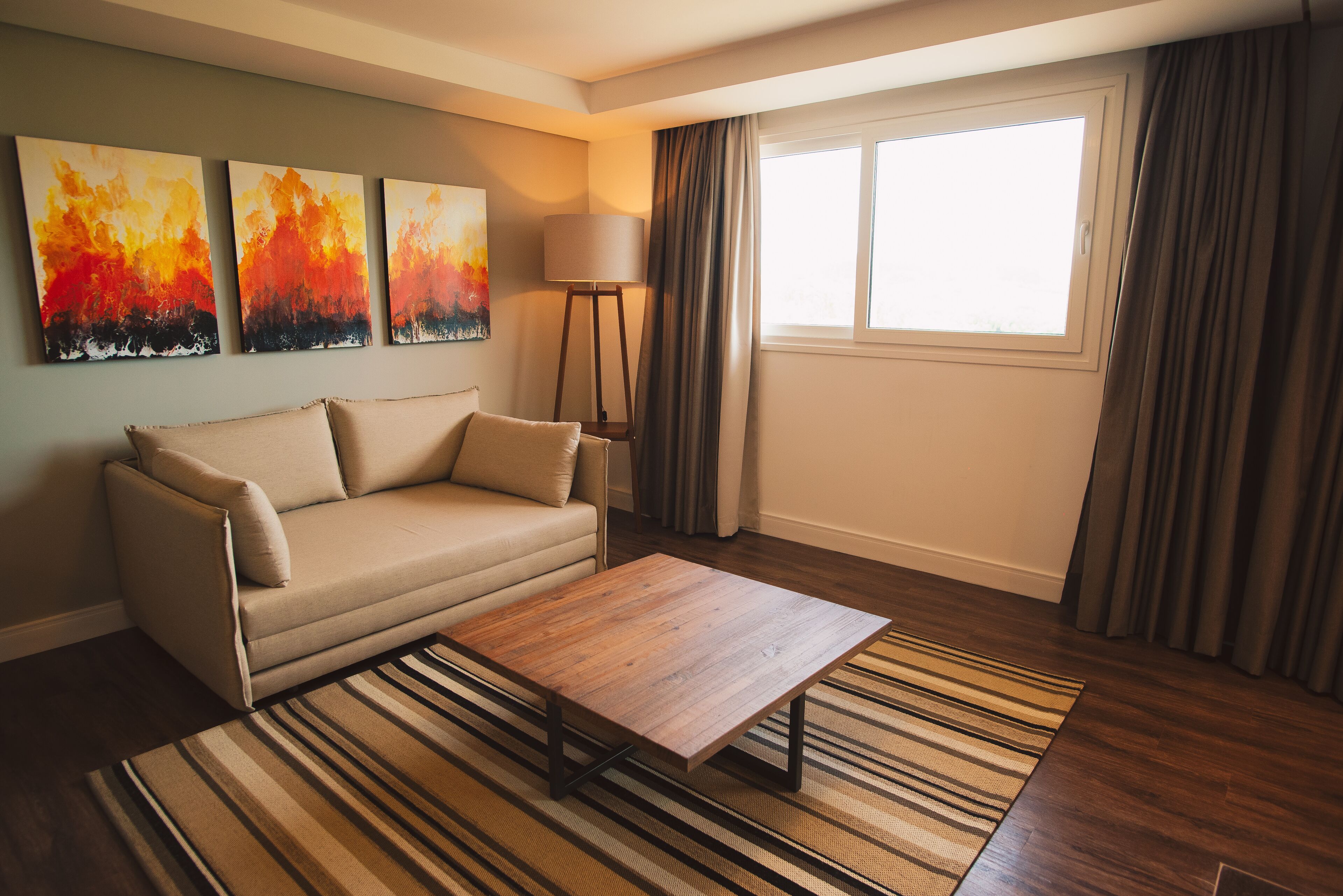 A living room with a sofa, a coffee table, a lamp, and three paintings on the wall.