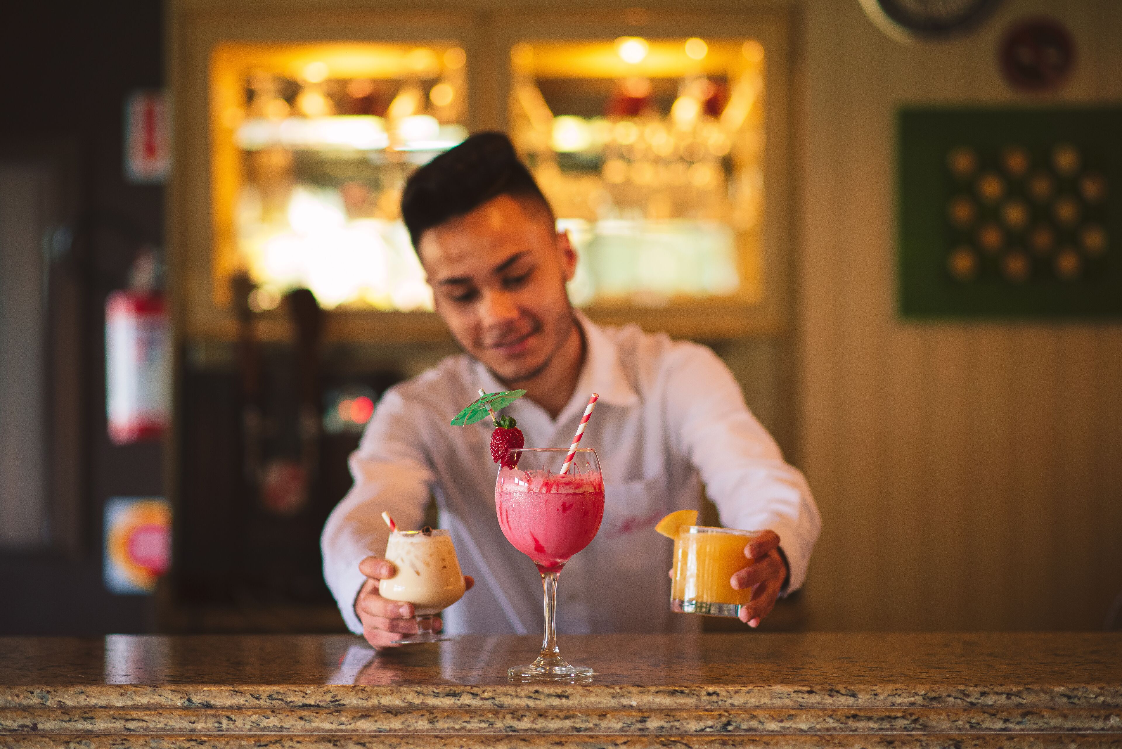 A bar setting with a person holding two drinks, one in a tall glass and another in a short glass.
