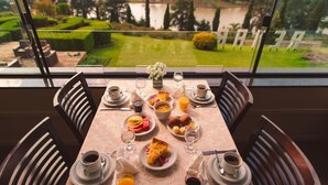 A dining table set with plates, cups, and glasses, overlooking a well-manicured garden with a lake view.