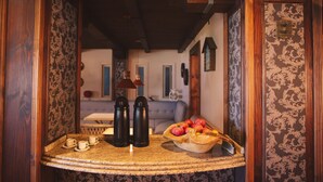 A wooden-framed room with a curved table holding cups, a bowl of fruit, and two thermos flasks.