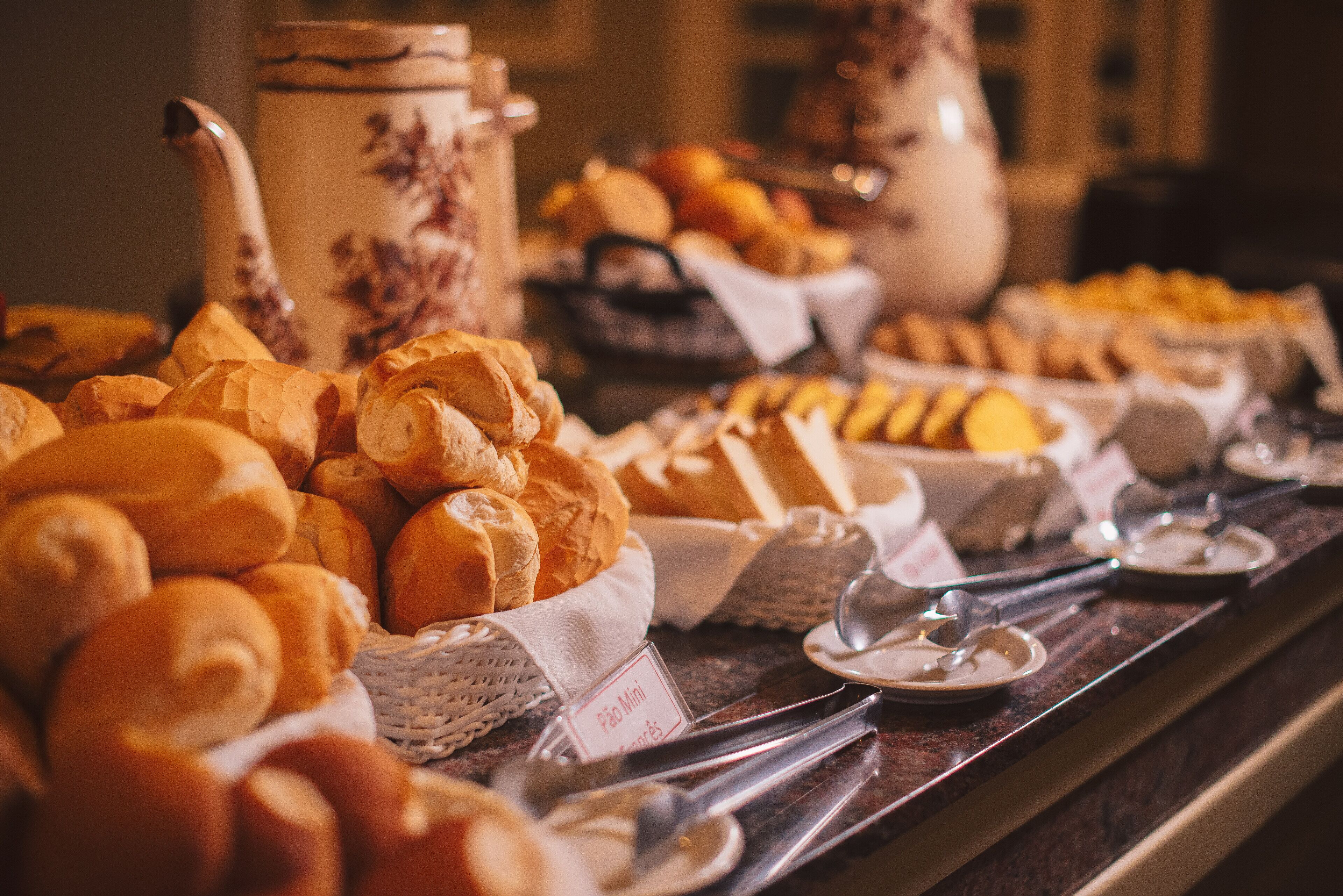 Un buffet proposant une variété de pains et de viennoiseries, notamment des croissants et des petits pains, disposés sur un comptoir avec les ustensiles nécessaires pour se servir.