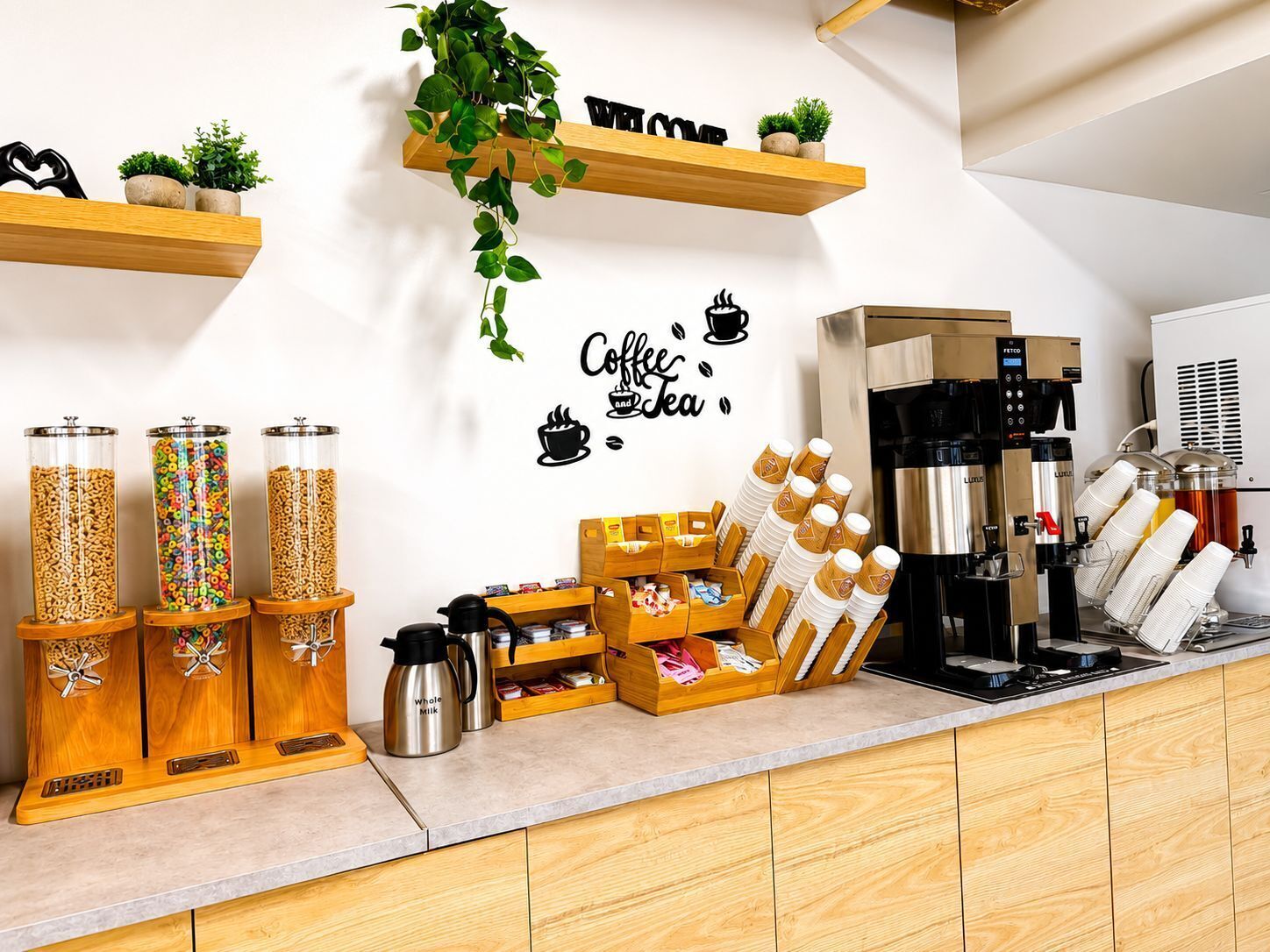 A coffee station with dispensers, a coffee machine, and a wall with a coffee and tea sign.