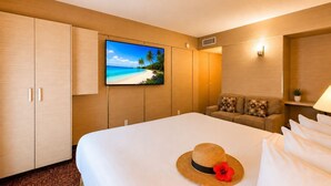 A hotel room with a bed, a sofa, a television, and a wall-mounted picture.