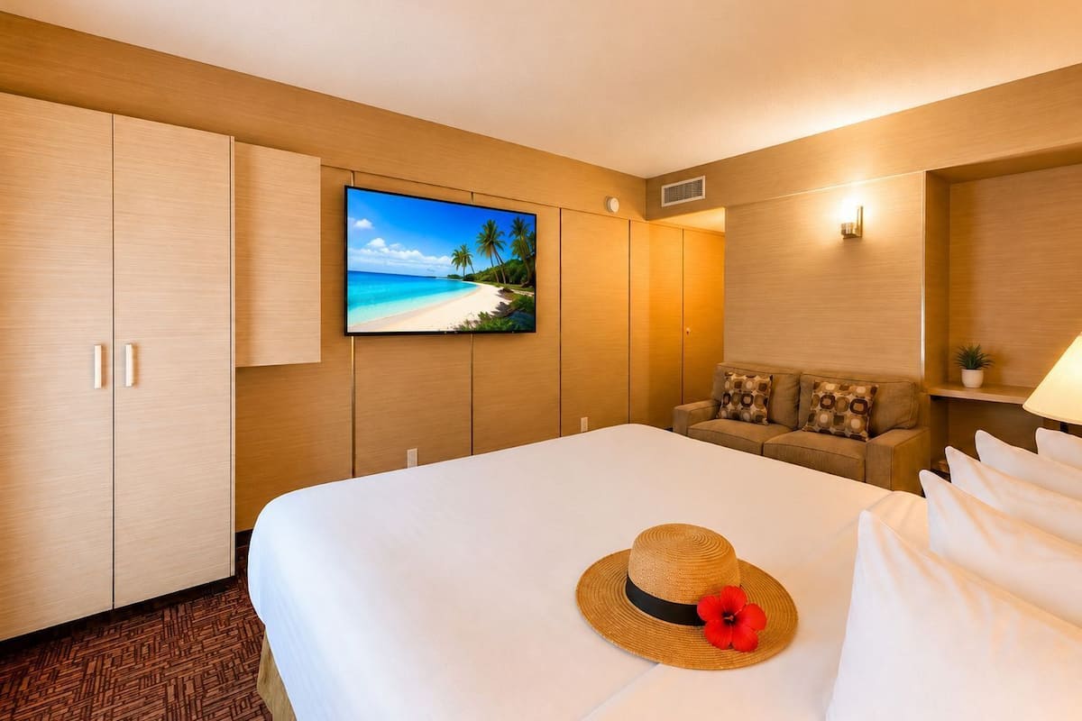Hotellihuone, jossa on sänky, sohva, televisio ja seinälle ripustettu taulu.