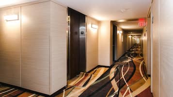 A hotel hallway with a carpeted floor, an elevator, and an exit sign.