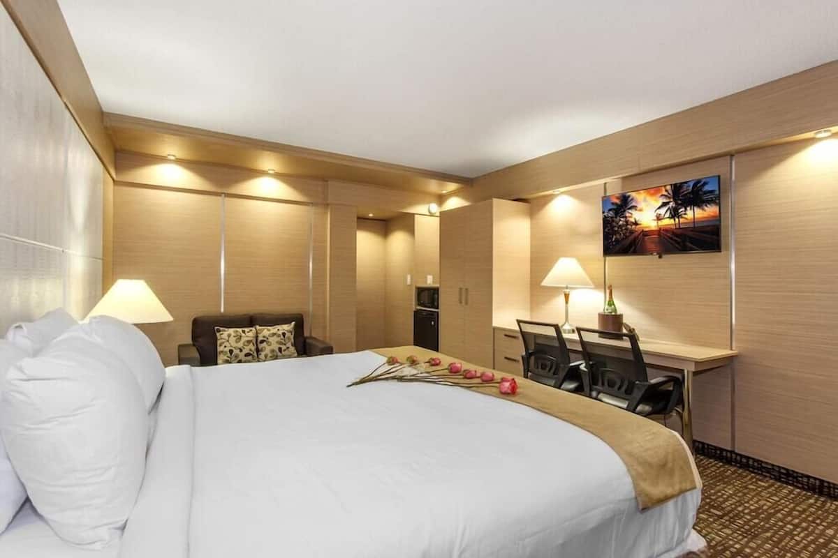 Hotellihuone, jossa on suuri sänky, työpöytä kahdella tuolilla, minibaari ja taulu seinällä.