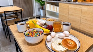 A breakfast table with cereal, eggs, juice, and a bagel.