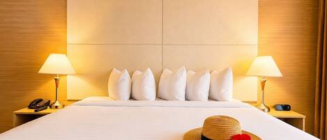 A hotel room with a large bed, two bedside lamps, a telephone, and a straw hat with a red flower on the bed.