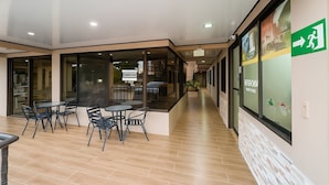 A hallway with a dining area featuring tables and chairs, a glass partition, and a green emergency exit sign. - Hotel del Rio (Liberia)