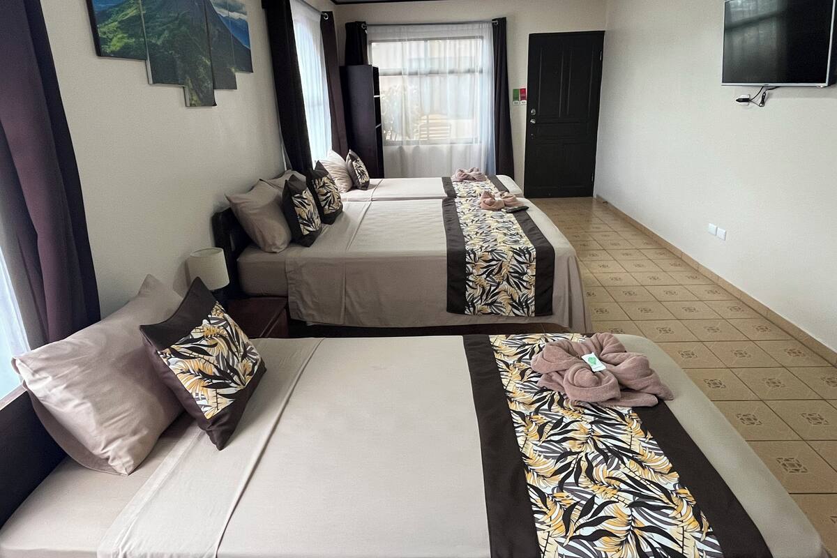 A hotel room with two beds, each with a patterned bedspread and pillows. There is a television mounted on the wall and a window with curtains.